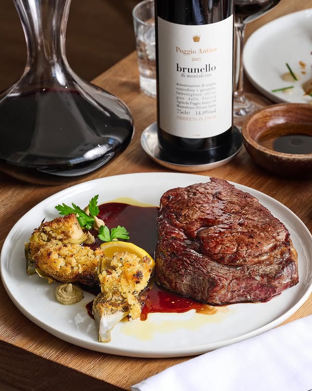 Grilled 15-oz ribeye served with breadcrumb-topped artichokes, with a bottle of 2017 Brunello in the background
