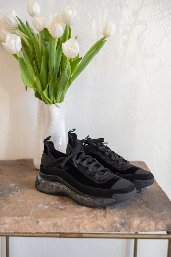 Photo of black vintage velvet Chanel trainers on a stone coffee table with a white vase filled with white tulips in the background