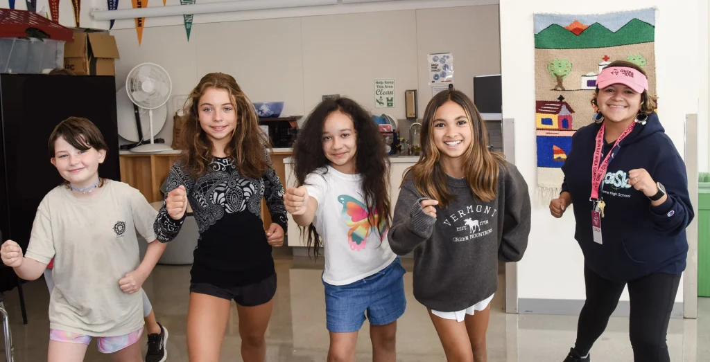 Four middle school students and their teacher in a classroom smiling and posing for camera