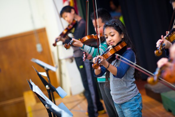 Three Elementary students playing the violin with sheet music in music class