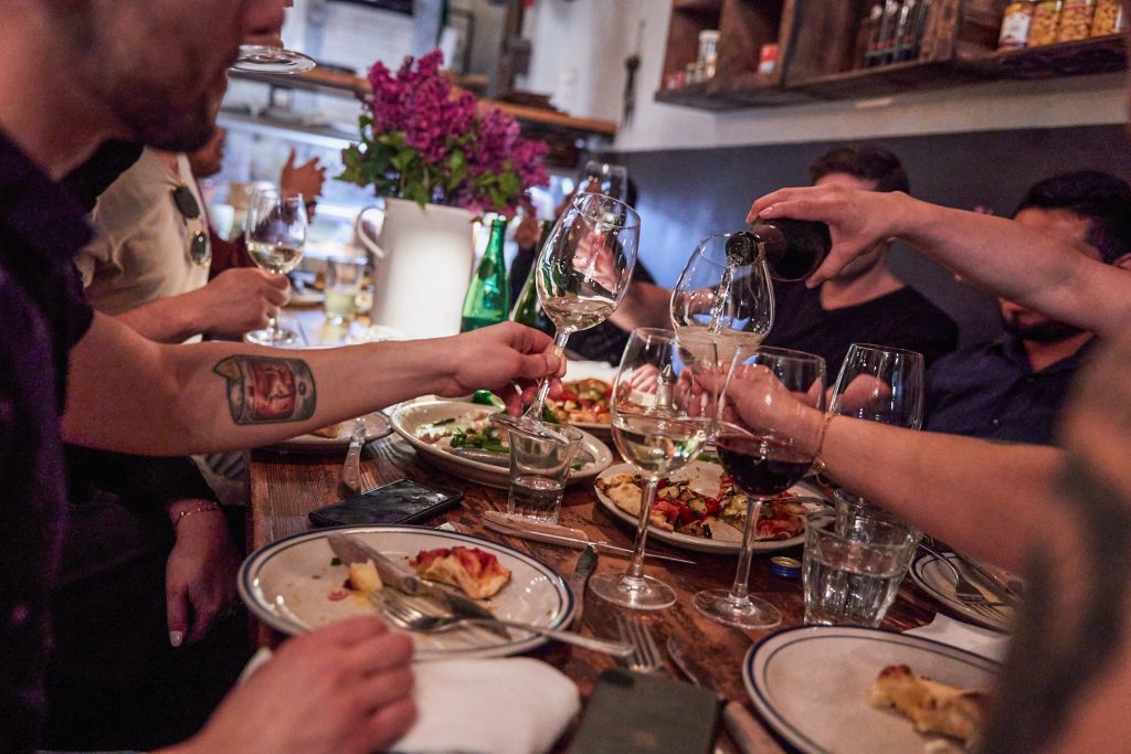 Group of male diners pouring and drinking glasses of wine and eating pizza and Italian appetizers at Montesacro SoMa