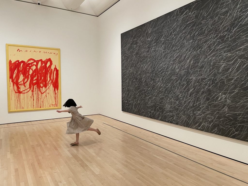 Young girl in a beige dress twirling in front of multiple large abstract paintings at the SF Museum of Modern Art