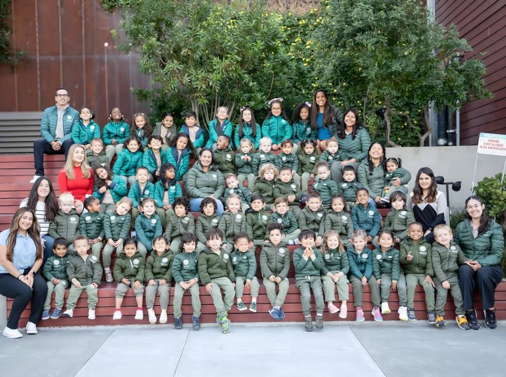Class photo of young students, teachers, and staff in green jackets outside of The Dahlia School
