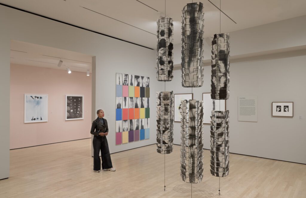 Woman in black leather jacket, blank pants, and white and tan sneakers admiring an art installation in an airy gallery space at SFMOMA