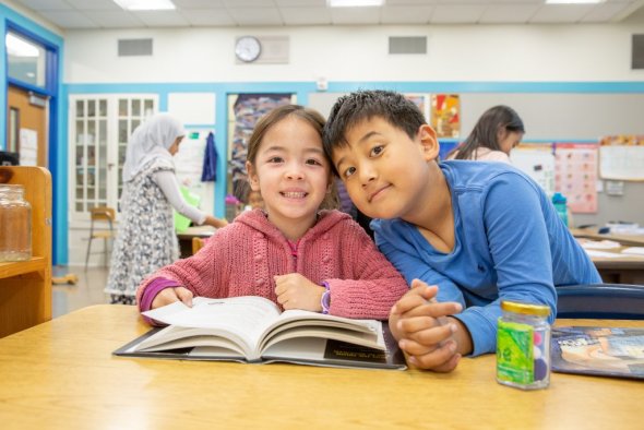 Two elementary students reading a book in a classroom