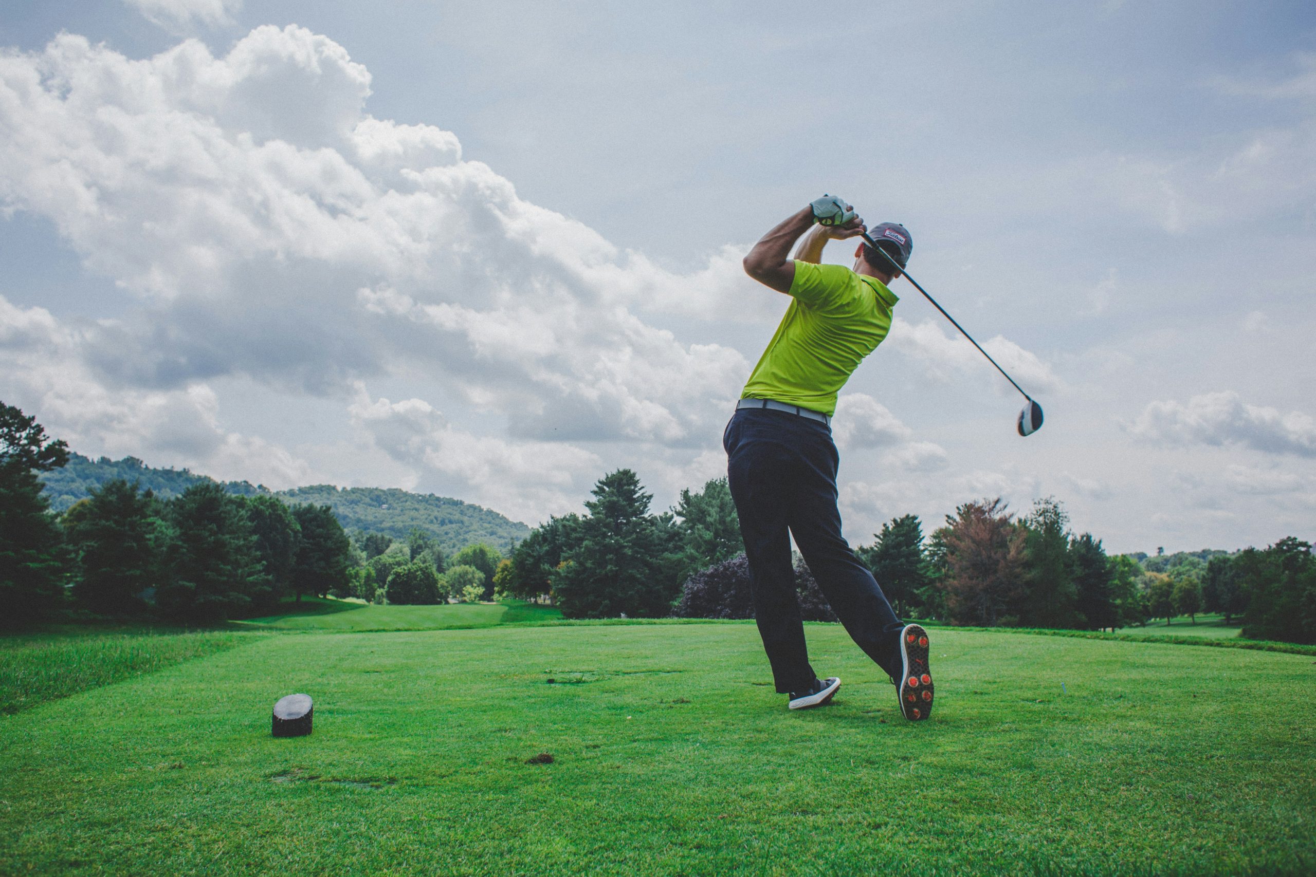 Golfer teeing off on a lush private championship golf course fairway under a bright sky