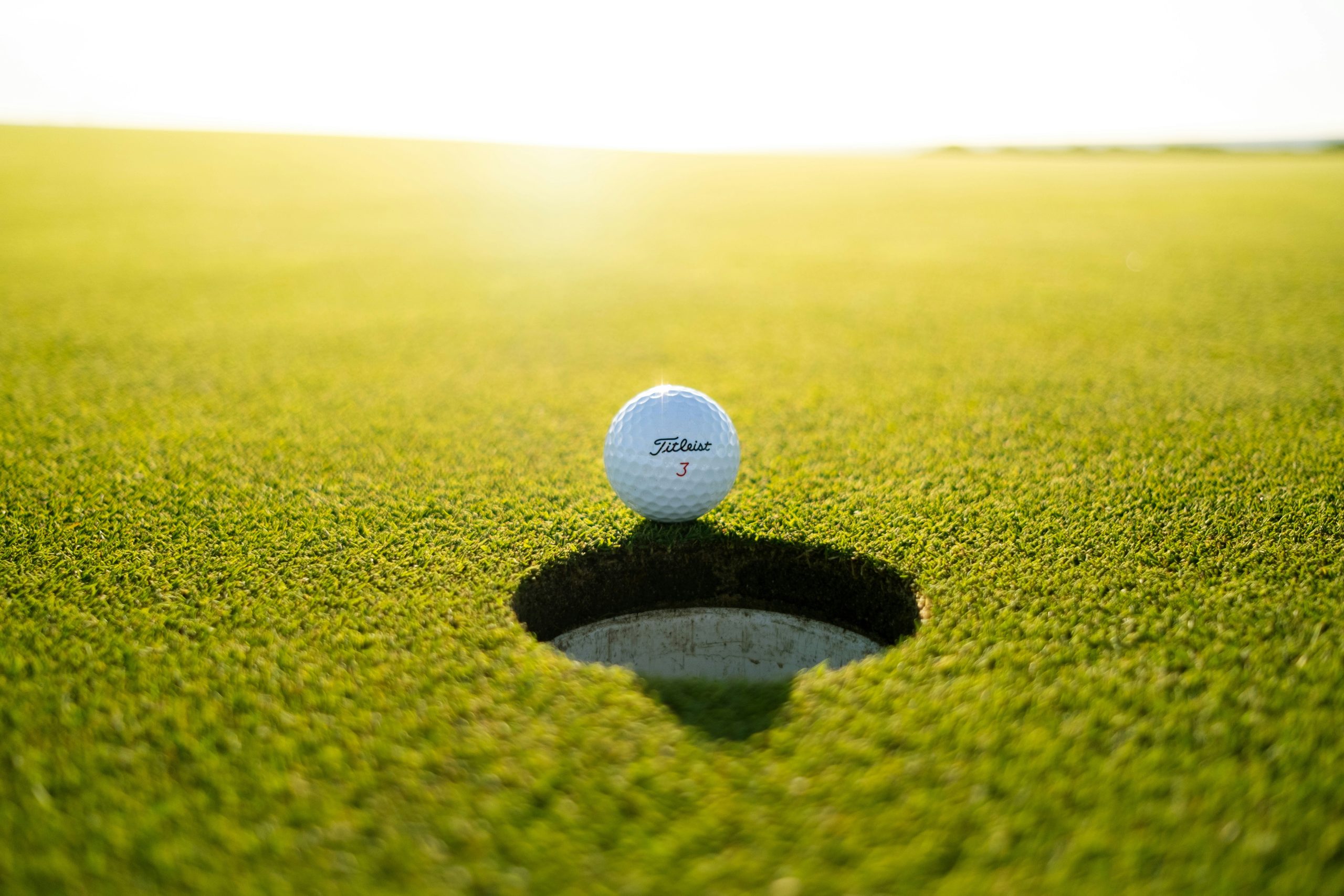 Golf ball resting on the edge of the cup on a manicured putting green at sunset