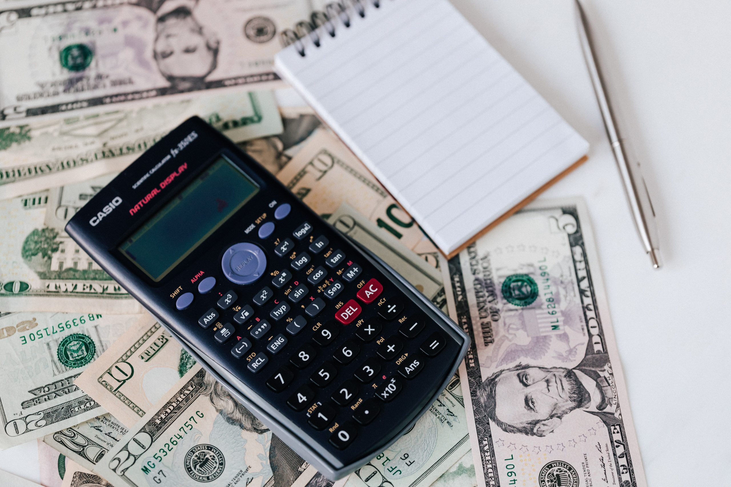 Calculator and notepad resting on a stack of U.S. dollar bills, illustrating a buyer estimating closing costs
