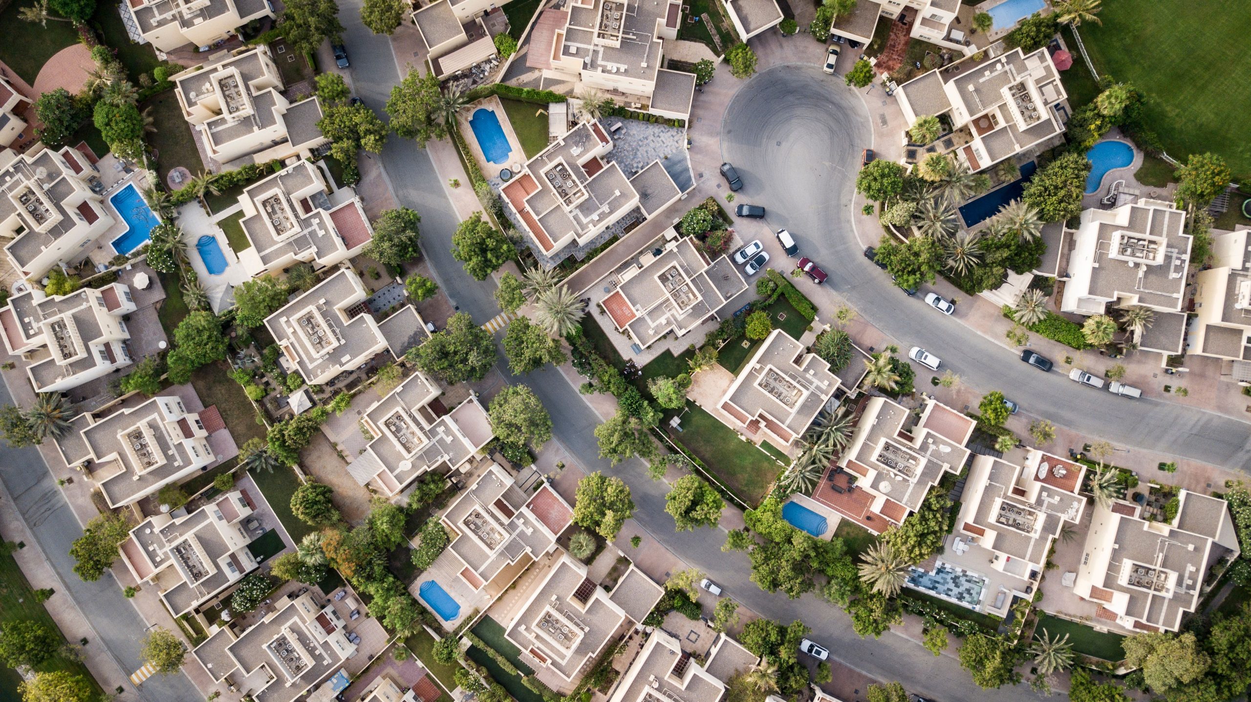 Aerial view of a gated residential community with landscaped grounds, winding streets, and private swimming pools