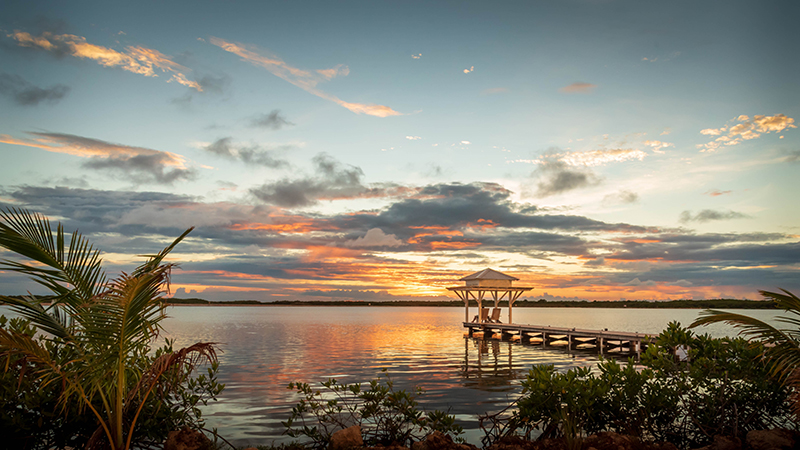 A view of a pier with bungalow at sunset in the Caribbean.