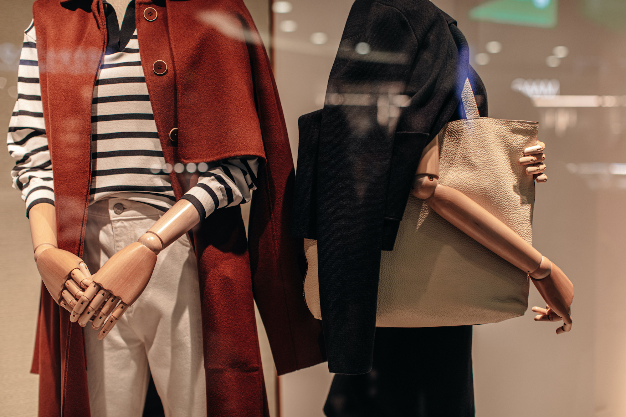 Two stylish mannequins in a store window dressed in seasonal fashion cloth. Brown and black jacket, white pants, beige leather bag