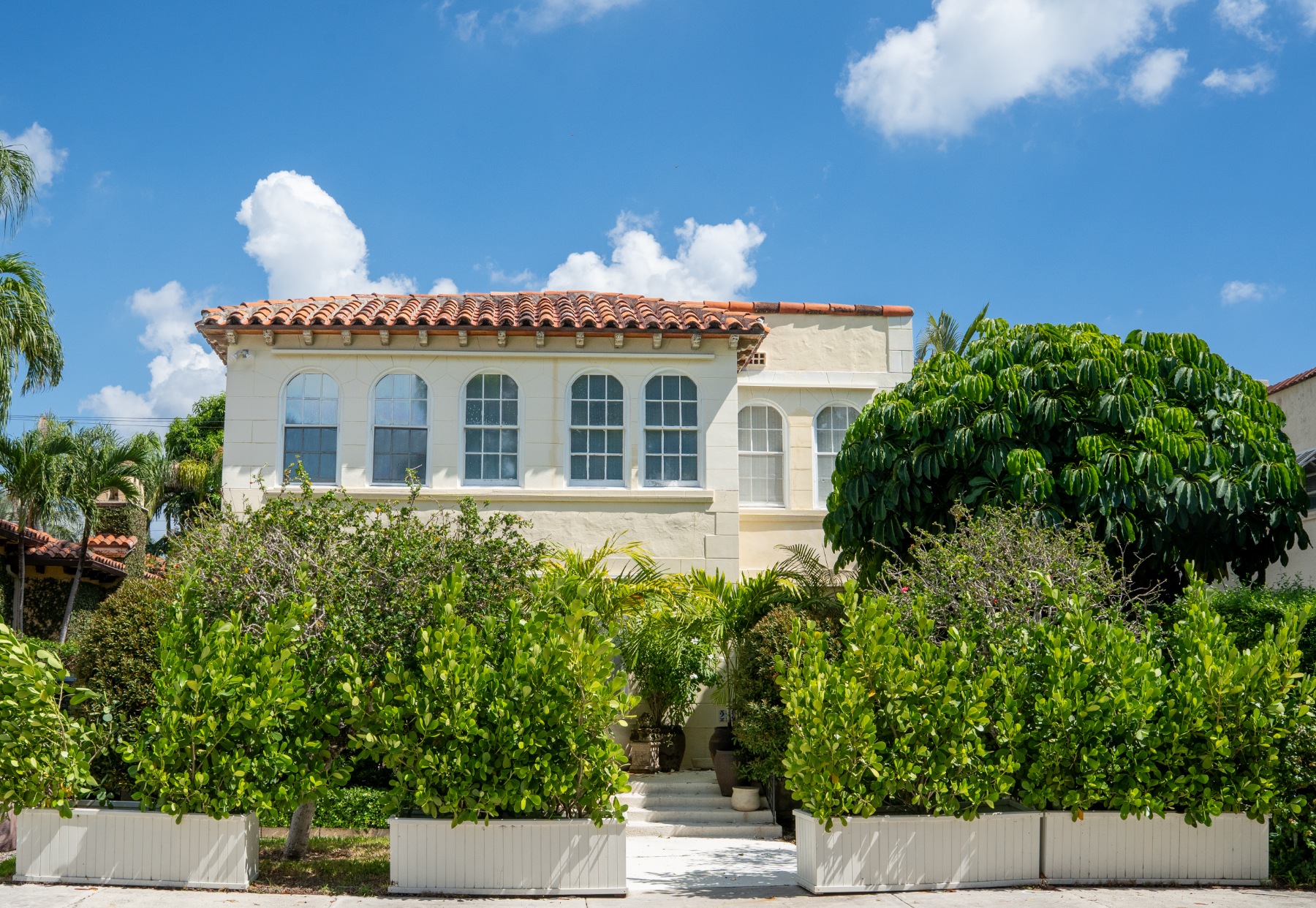 Mediterranean-style home with red tile roof, hedge-lined entry, and gated front path