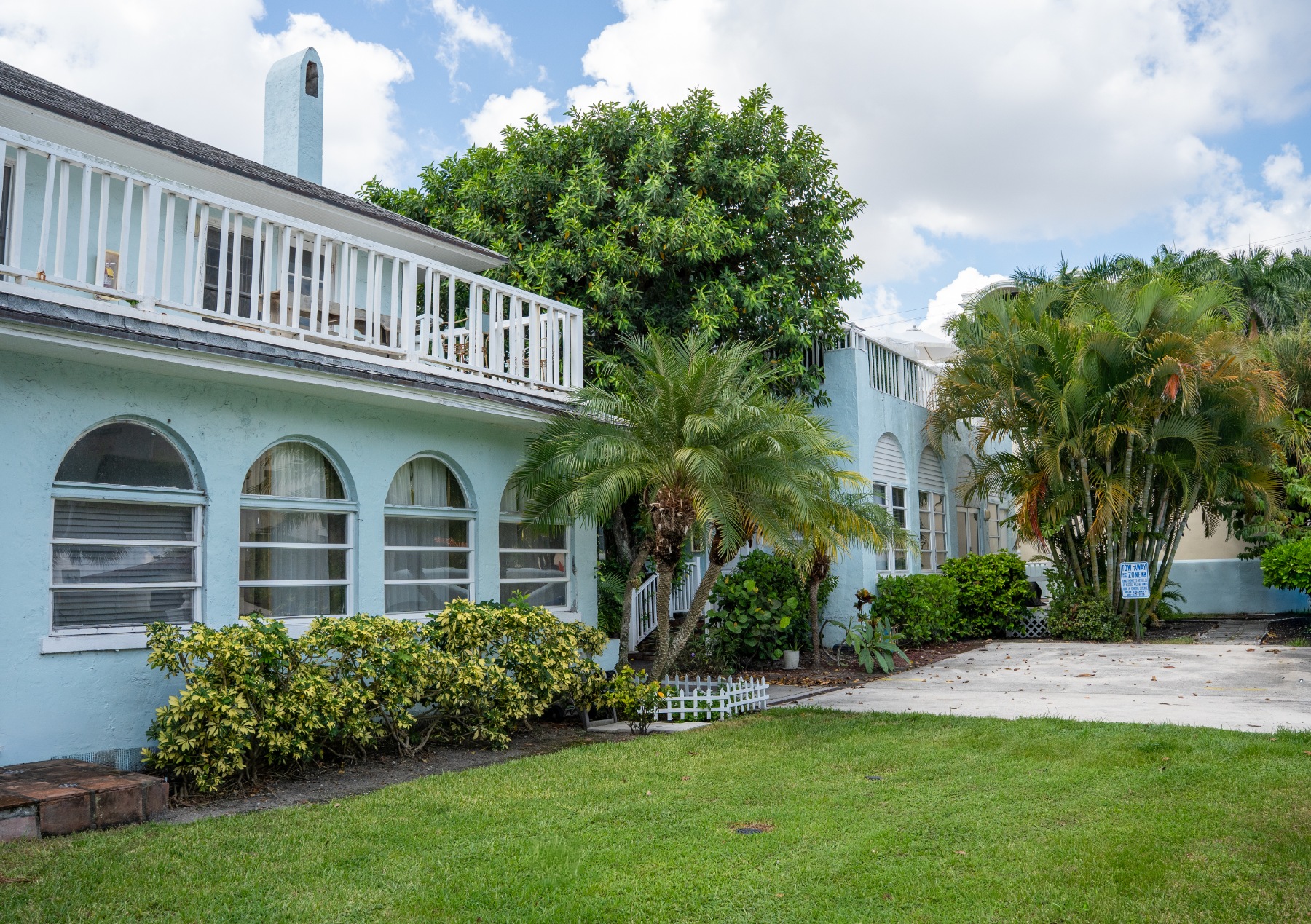 White stucco home exterior with balcony, arched doorway, and front lawn