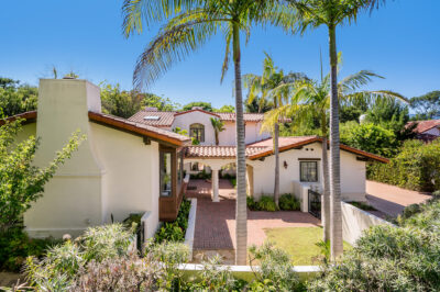 A home with palm trees and lush landscaping, featuring a front porch