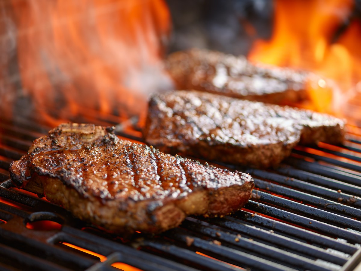 Grilling steaks on flaming grill and shot with selective focus