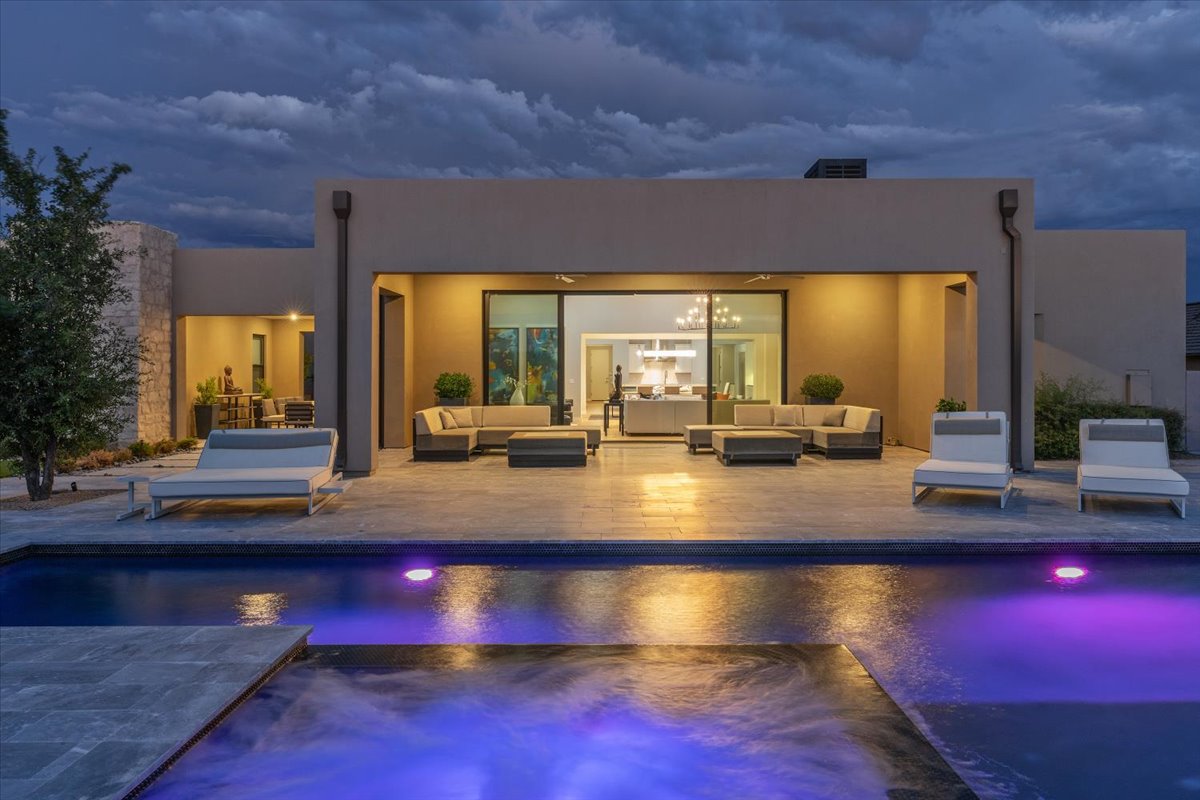 Evening view of a Bronco Estates home by Camelot Homes, featuring a modern patio area with lounge seating and an illuminated pool.