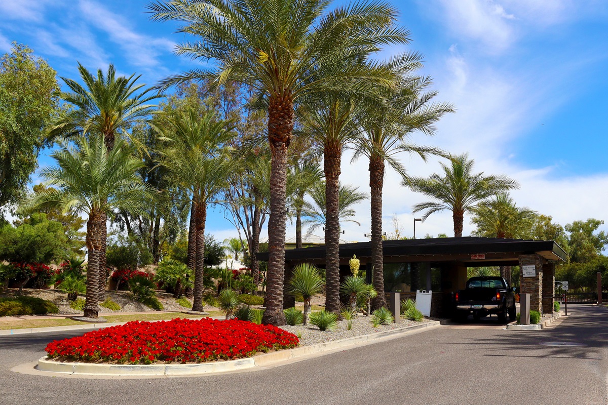Guard gate entrance at Gainey Ranch in Scottsdale, framed by tall palm trees and vibrant red flowers.