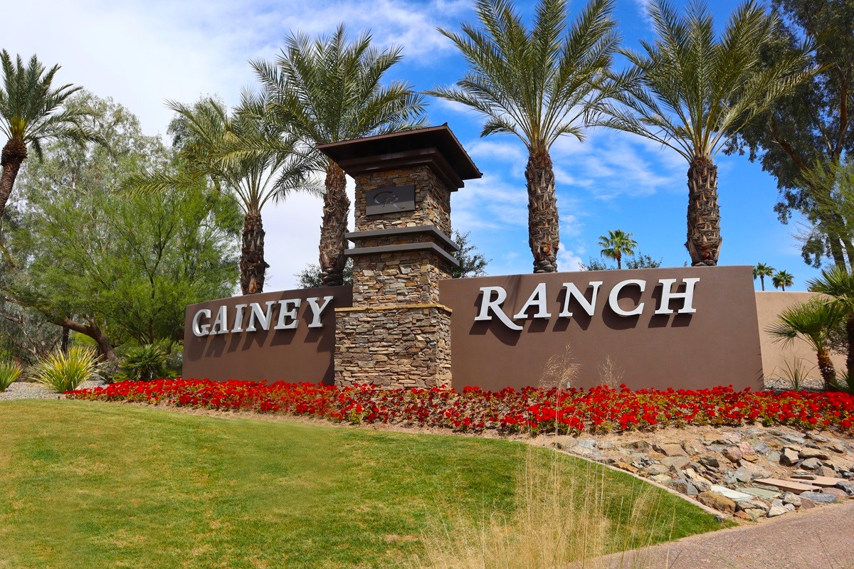 Gainey Ranch entrance sign with stone accents, palm trees, and colorful flower beds in Scottsdale.