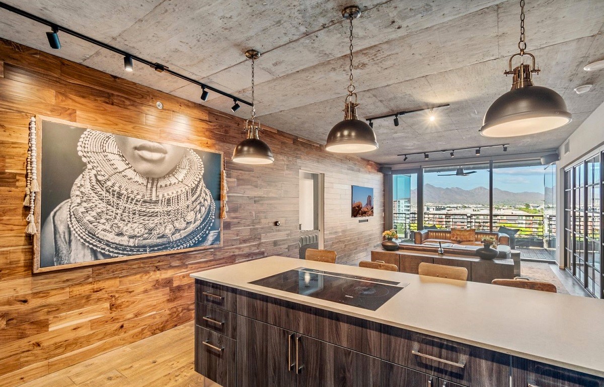 Modern kitchen and living area at Optima Kierland with industrial decor, wood paneling, and mountain views through large windows.