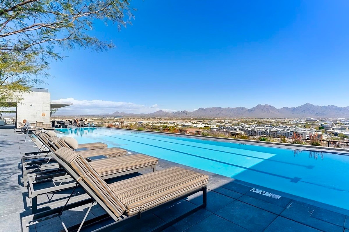 Rooftop pool at Optima Kierland with lounge chairs, cityscape, and mountain views under a clear blue sky.