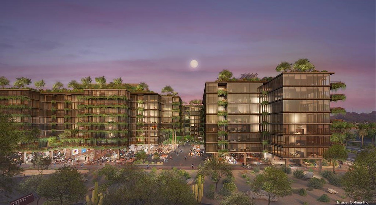 A nighttime view of Optima McDowell Mountain with glass-fronted buildings surrounded by lush greenery, featuring a spacious outdoor plaza lit by ambient lights.