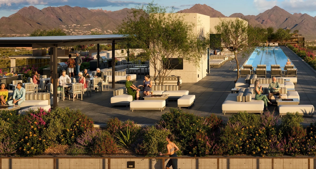 A rooftop lounge at Optima McDowell Mountain with seating areas, landscaped greenery, and an elongated pool, set against a backdrop of desert mountains.