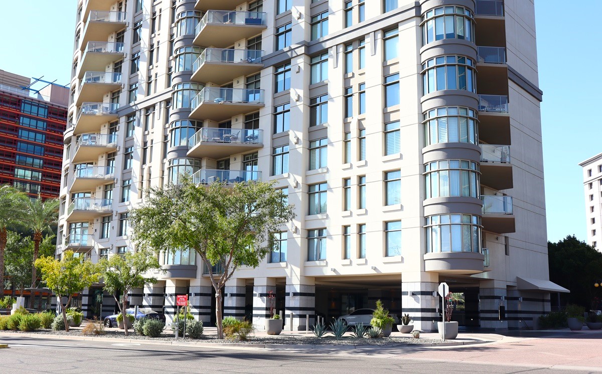 Exterior view of Esplanade Place, showing a modern high-rise with glass balconies, surrounded by landscaped greenery and trees.