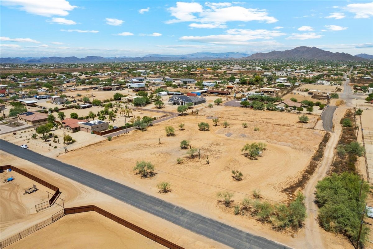 Aerial view of a residential neighborhood in a desert area, with scattered homes, dry terrain, and distant mountains.