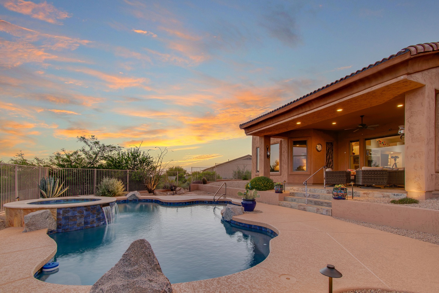 A luxury home with a pool and spacious patio, set against a colorful sunset sky.