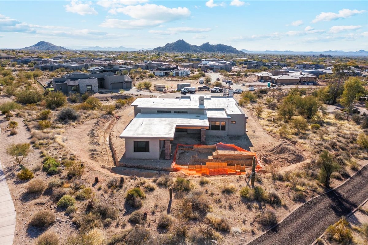 A luxury home under construction in a scenic desert community, surrounded by natural landscape and mountain views in the distance.