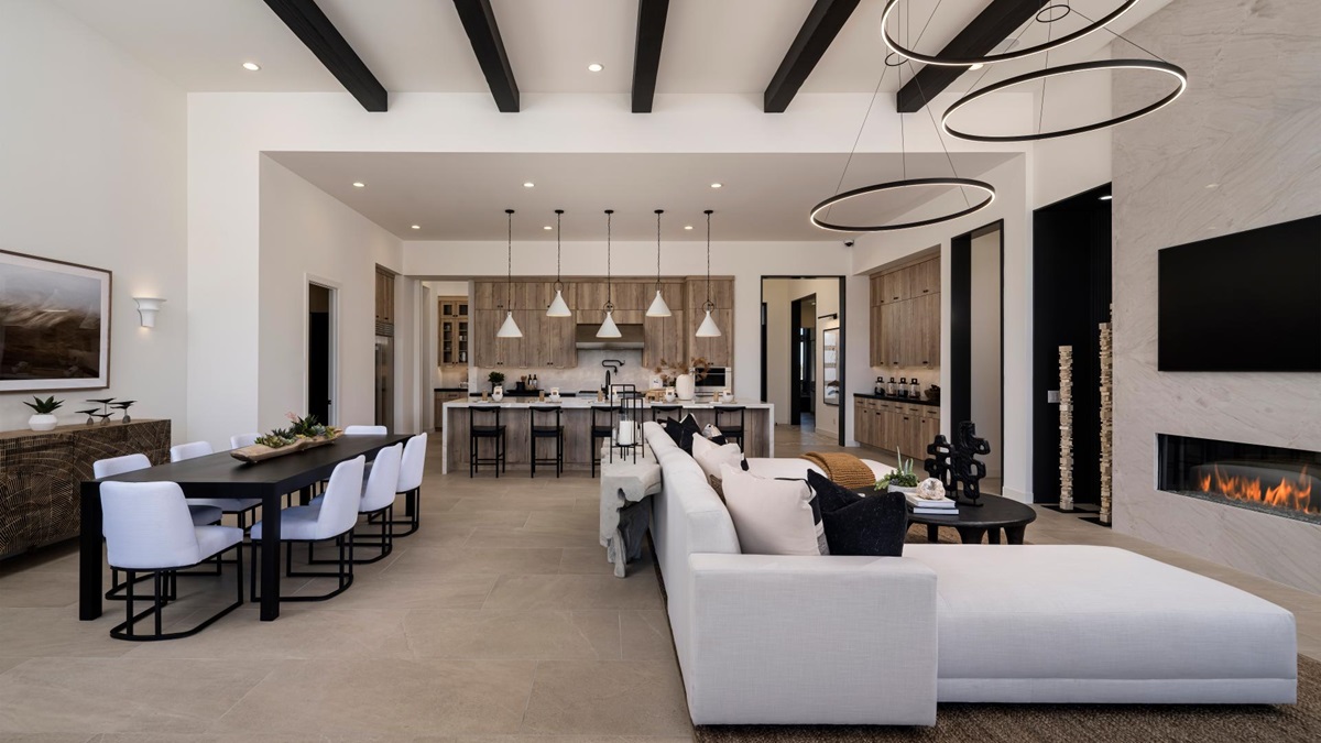 Spacious modern living area with high ceilings, exposed beams, a sleek kitchen island with pendant lighting, and a cozy seating area near a contemporary fireplace.