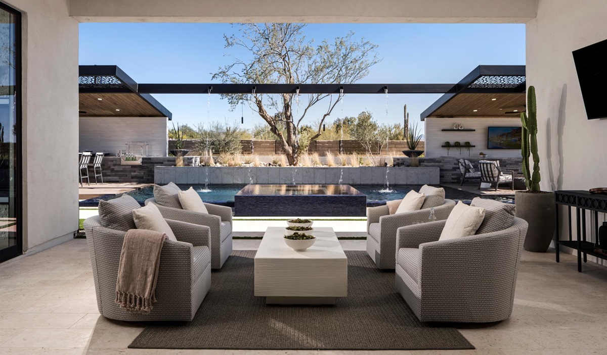 Outdoor patio with comfortable seating overlooking a luxurious pool and water feature, with a shaded dining and entertainment area in the background.