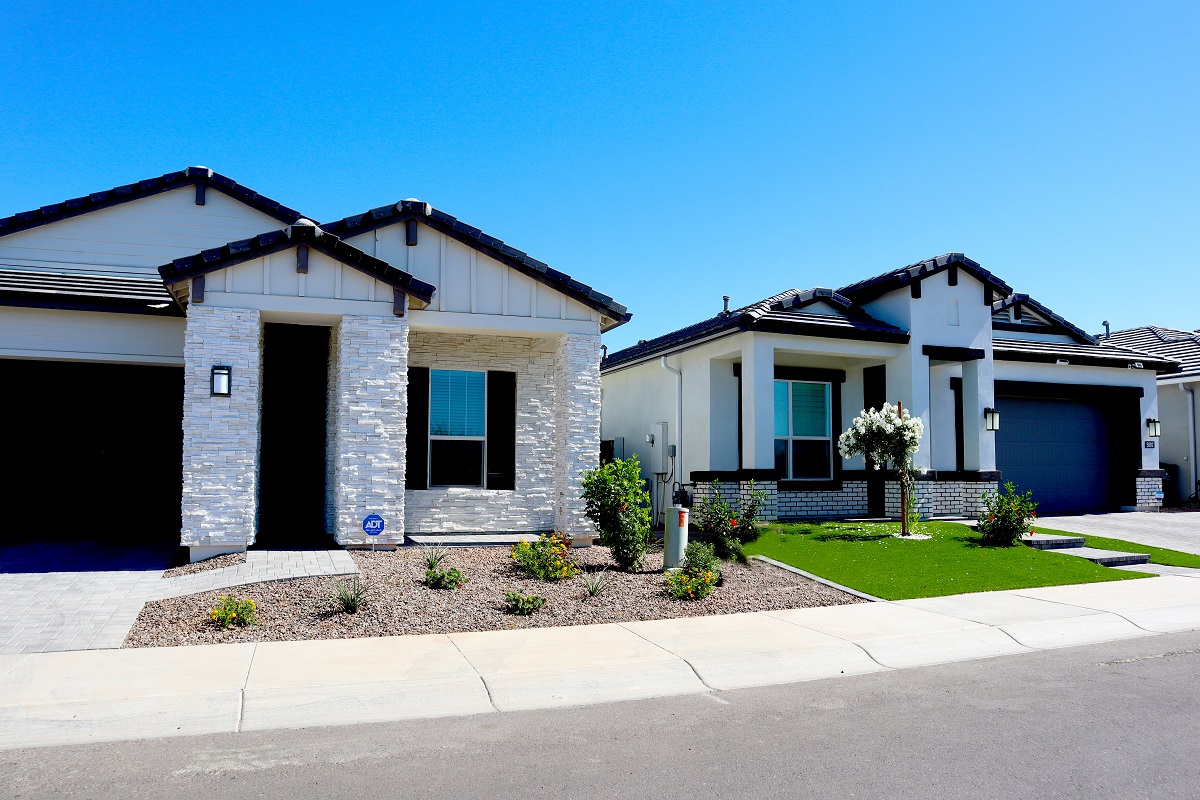 Two modern single-story homes with stone and brick accents. Clear, sunny day.