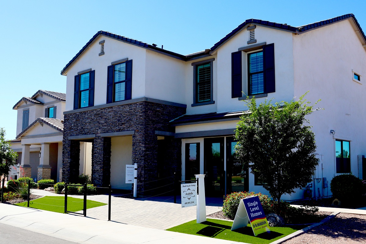 Two-story house with stone accents, blue shutters, and a small yard with signs. Sunny day.