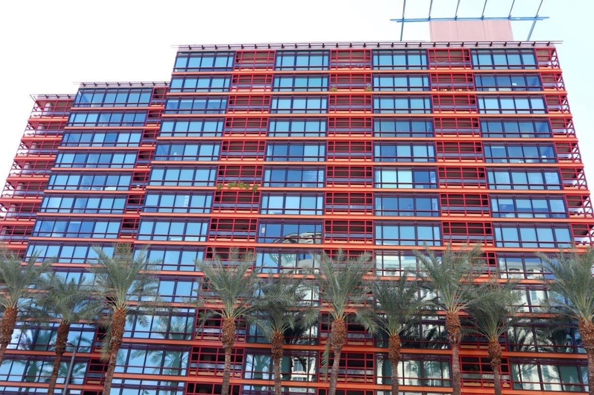 Exterior view of Optima Biltmore, a vibrant red-framed condo building with large glass windows and palm trees lining the front, creating a striking urban facade.