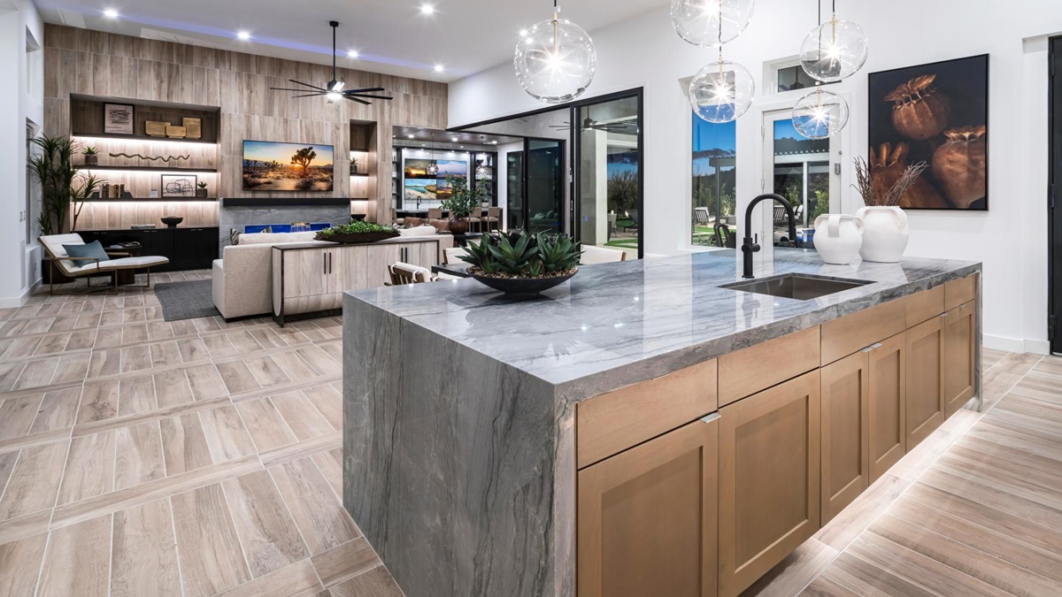 Modern kitchen with a large marble island, open shelving, and adjacent living room featuring wood accents, built-in lighting, and outdoor access.