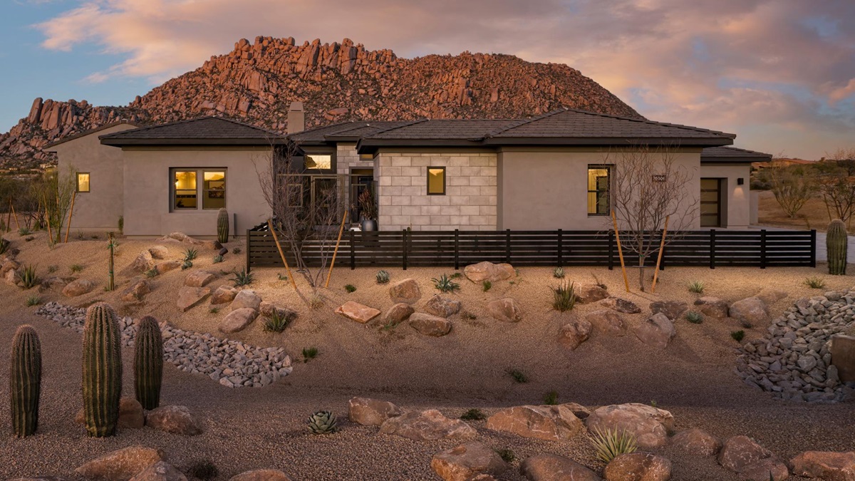 Single-story desert home with a modern exterior, surrounded by natural desert landscaping and scenic rocky mountain views in the background.