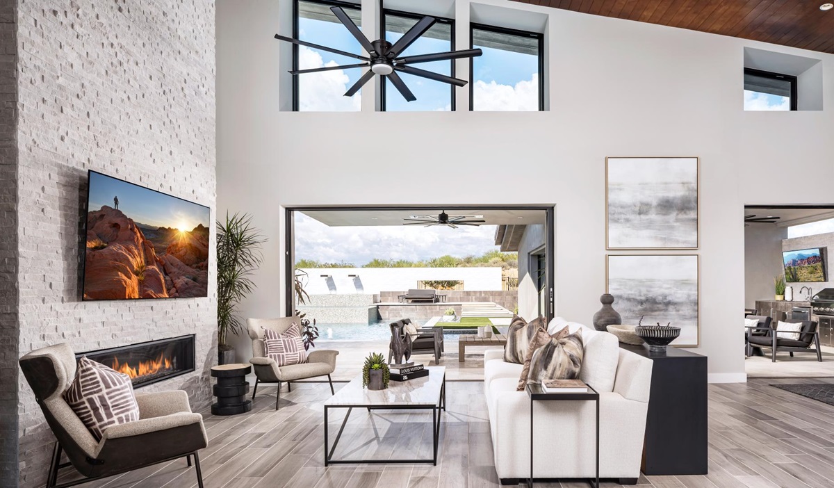 Modern living room with high ceilings, a fireplace, and large doors opening to a pool area.