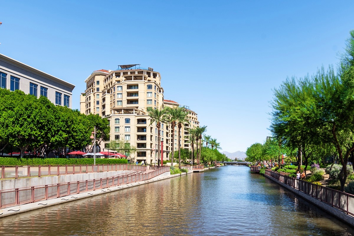 Canal lined with luxury condos and palm trees in Old Town Scottsdale under a clear blue sky.