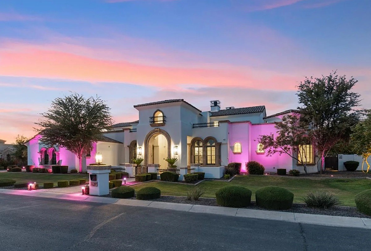 Luxury home exterior at sunset with vibrant pink smart lighting illuminating the landscape and architectural features, showcasing modern smart home technology.