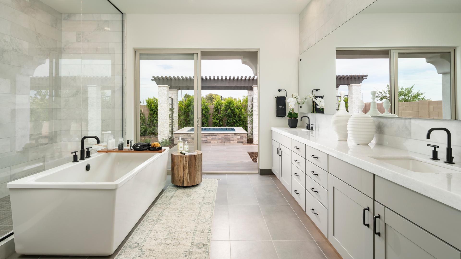 Luxurious bathroom with a freestanding tub, double vanity, and large glass doors opening to a private outdoor patio with a pergola and spa view.