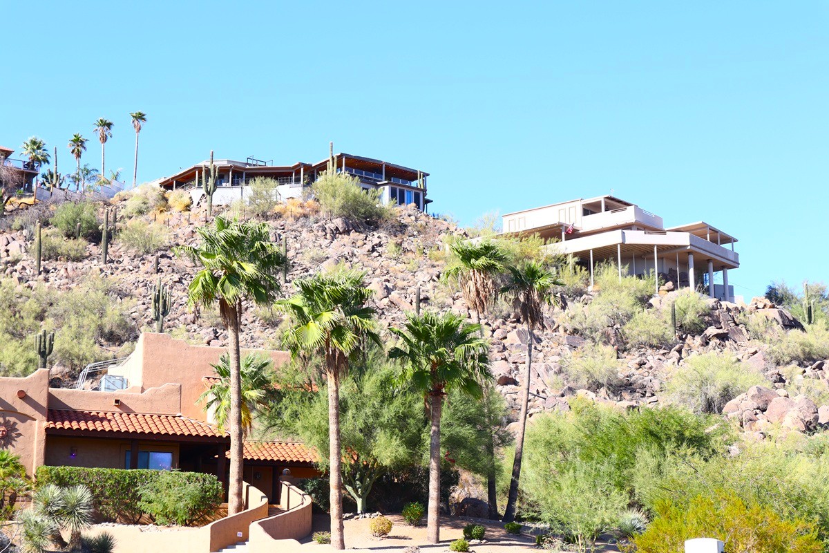 Luxury homes perched on rocky hillsides in Paradise Valley, Arizona with desert landscaping and palm trees in the foreground.