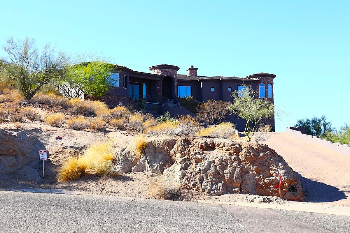 Elegant desert-style home with a brick driveway surrounded by natural desert vegetation in the Arizona town of Paradise Valley.