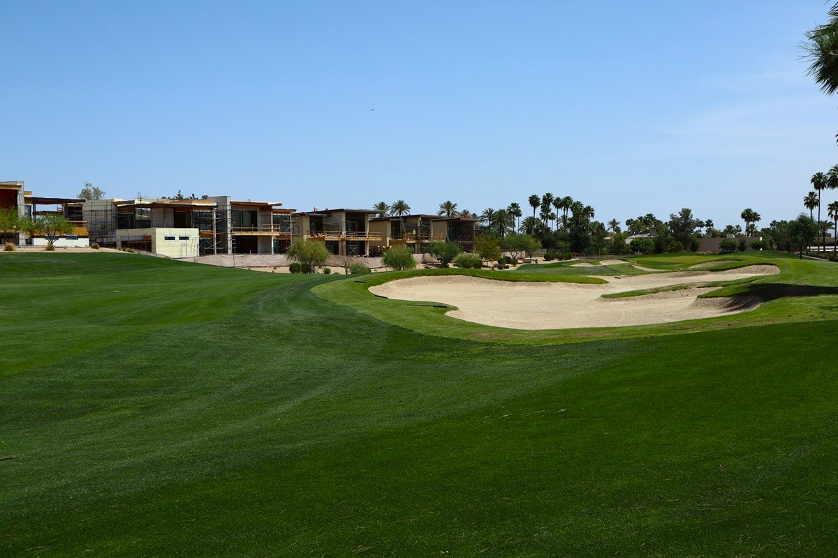 Luxury homes under construction next to a golf course with green grass and sand bunkers.