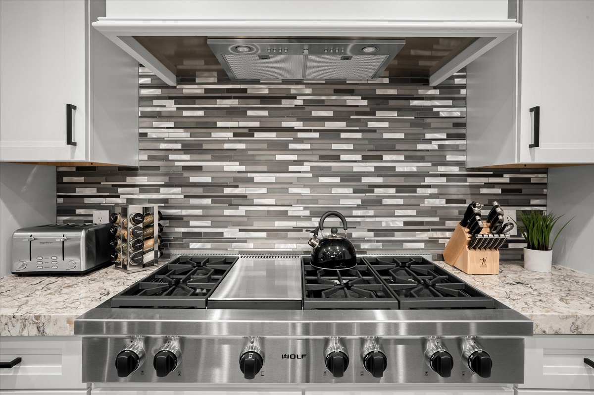 Modern stainless steel stove with sleek tile backsplash.
