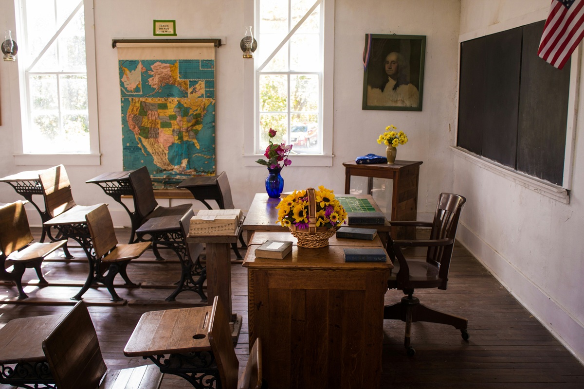 Vintage classroom with wooden desks, a map, and flowers on the teacher's desk.