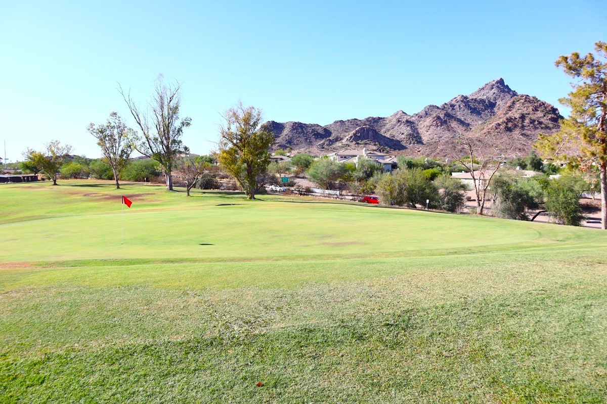 Golf course green with a red flag, mountain backdrop, and surrounding desert landscape.