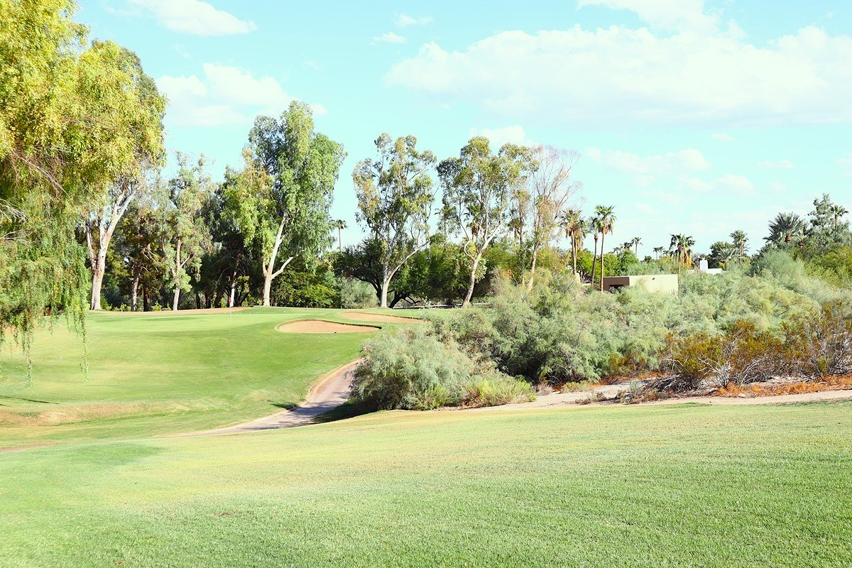 Golf fairway with sand bunker, lush greenery, and desert plants along the edges.