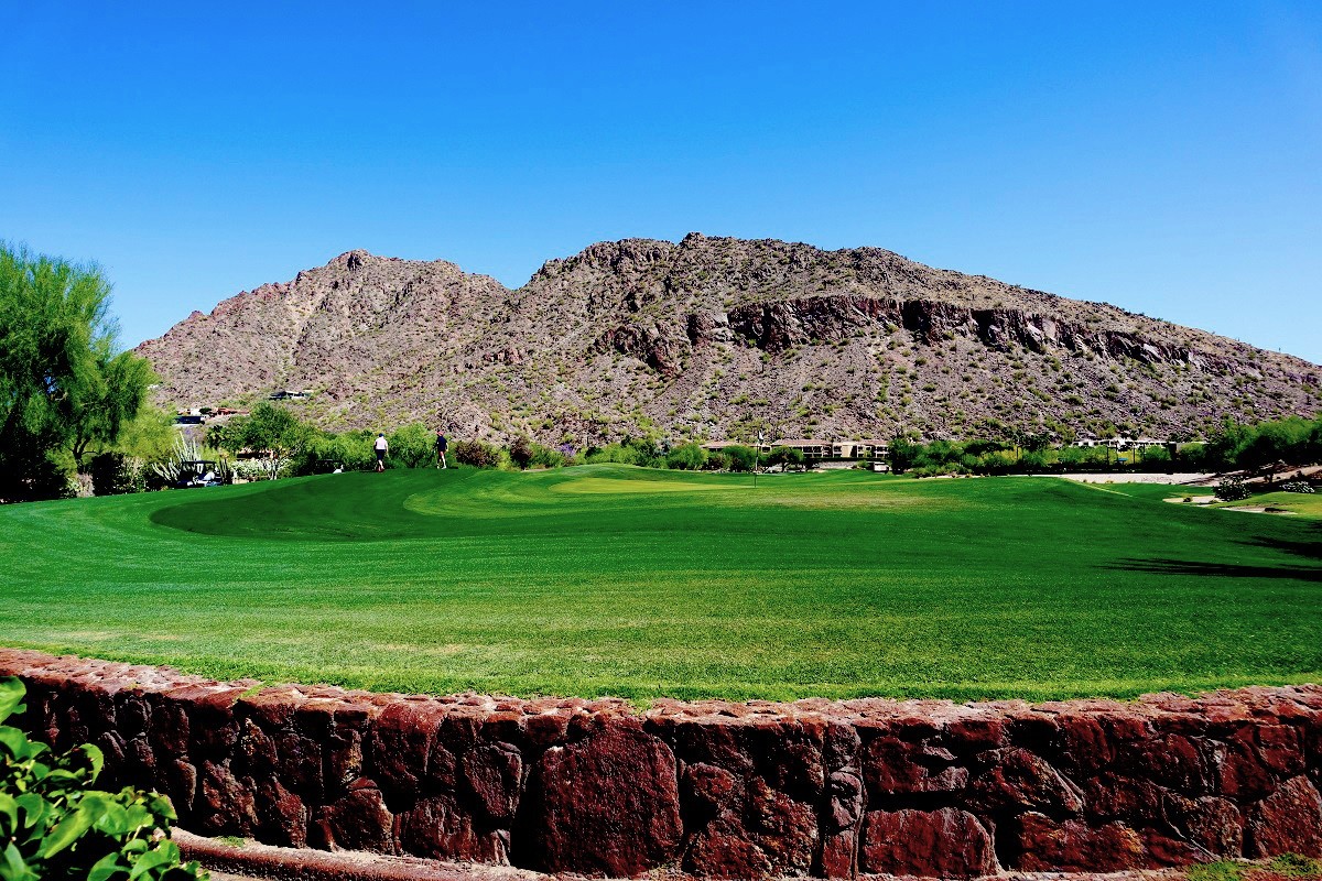 A beautiful green golf course with a blue sky and mountain in the background.