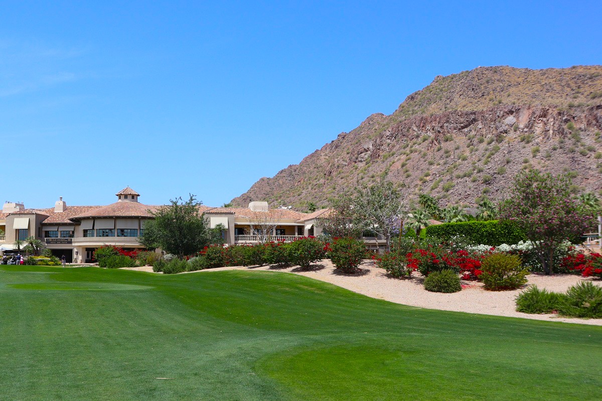 A beautiful green golf course with a blue sky and mountain in the background.